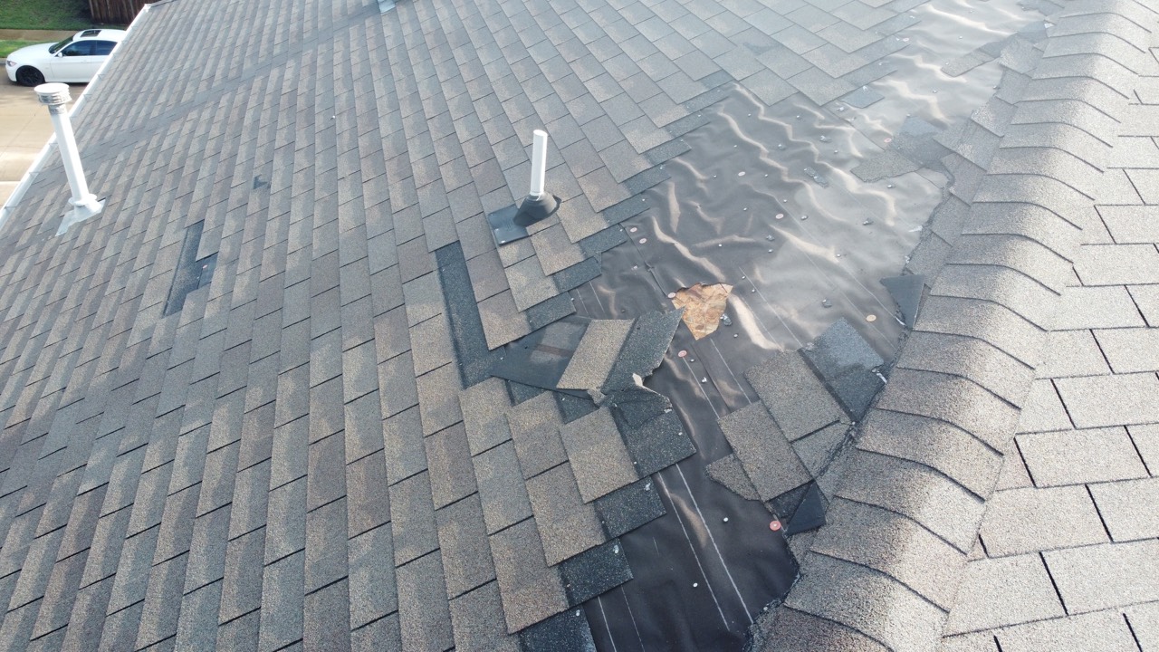 Storm-blown shingles exposing roof underlayment, captured by drone